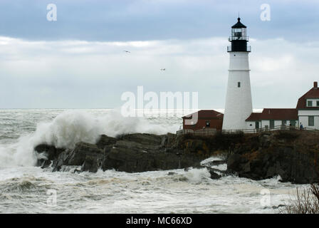 Sun breaks through the storm clouds as huge waves crash by Portland Head lighthouse in Maine during high tide. Stock Photo