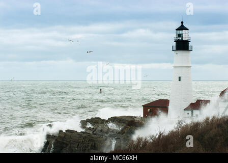 Surf creates huge waves crashing by Portland Head lighthouse as sun break through clouds in after late winter storm passes by. Unique high tides. Stock Photo