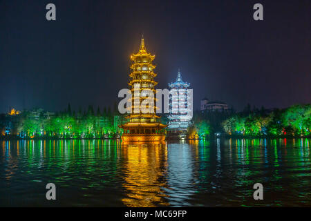 The Sun and Moon twin pagodas stand beautifully illuminated at night on Lake Shan. Guilin, China. Lights cast a wonderful reflection across the lake. Stock Photo