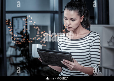 Serious cute woman holding a cup and using her tablet. Stock Photo