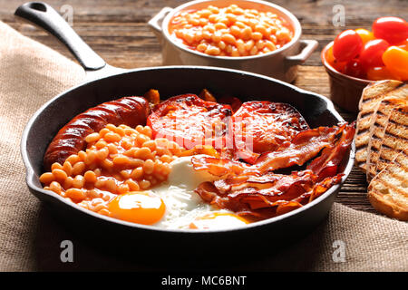 English Breakfast with sausages, grilled tomatoes, egg, bacon and beans on frying pan. Stock Photo