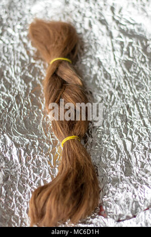 Braid hairstyle. Natural, healthy and red-haired hair on aluminum foil. Stock Photo