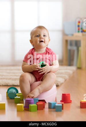 Little child girl sits on chamber pot, toilet, playing with toys Stock Photo