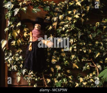 Poppet hanging against a wooden lattice wall with ivy trailing over it. The poppet, or curse doll, was widely used in sympathetic curse-magic. Traditionally made of wax or from the humanoid root of a mandrake. The curse, or death-wish, is usually written on an attached sheet of paper or vellum. Stock Photo