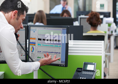 Businessman On Phone Using Computer In Busy Office Stock Photo