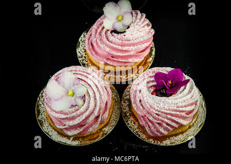 top view on three pink zephyr cookies decorated with violet and white flowers on black mirror background from above Stock Photo