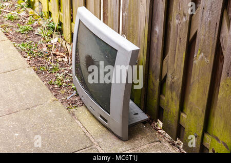 broken TV placed against a wooden fence Stock Photo