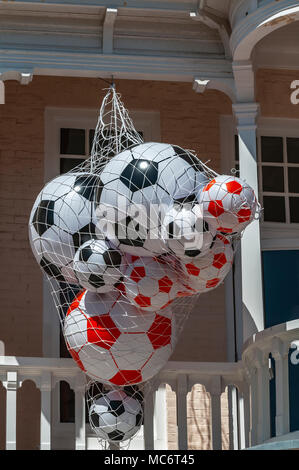 many types and sizes of plastic footballs in a net hanging on a wooden beam Stock Photo