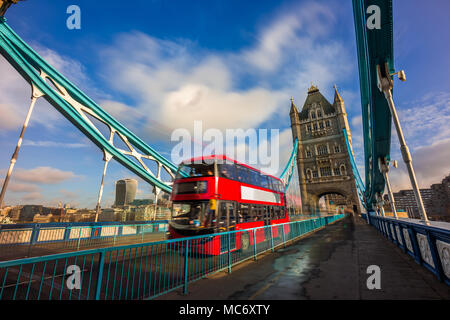 London, England - Iconic red double-decker bus in motion on famous Tower Bridge with skyscraper of Bank District at background. Blue sky and clouds Stock Photo