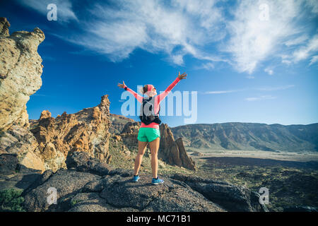 Woman hiker with arms outstretched in mountains reached life goal. Female runner or climber with hands up enjoy inspirational landscape on rocky trail Stock Photo