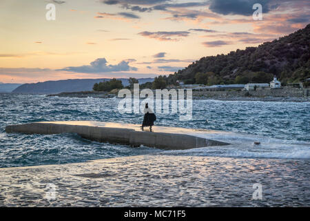 A monk from St. Panteleimon Monastery on Mount Athos watches the sunset from the quay.  Athos peninsula, Chalkidiki, Macedonia, Northern Greece. Stock Photo