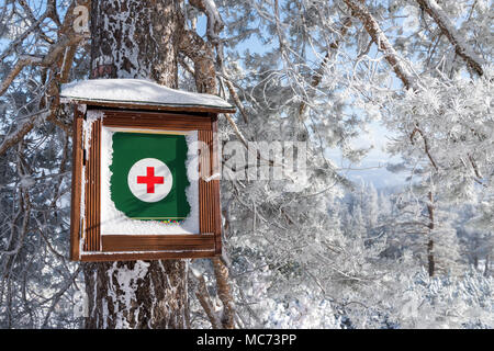 Wooden box for medical emergency first aid kit hanging on snow covered coniferous tree trunk in winter forest Stock Photo