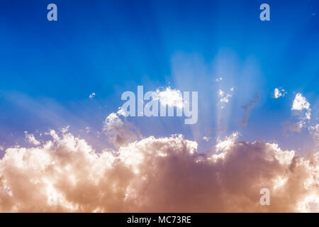 Sun behind vibrant colorful clouds and sunbeams in the blue sky with copy space, inspirational background Stock Photo