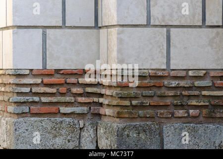 Weathered brick wall made of blocks with various color and size, large white blocks on top, small red bricks in middle and gray blocks on bottom Stock Photo