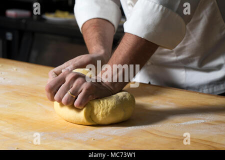 a closeup of a man kneading a ball of dough made with flour and eggs on a wooden board Stock Photo