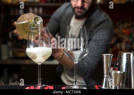 closeup of a barman working behind a bar counter, pouring prosecco in two wine glasses with focus on the glasses Stock Photo