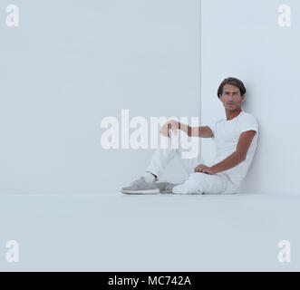 sad young man sitting beside a white wall .photo with copy space Stock Photo