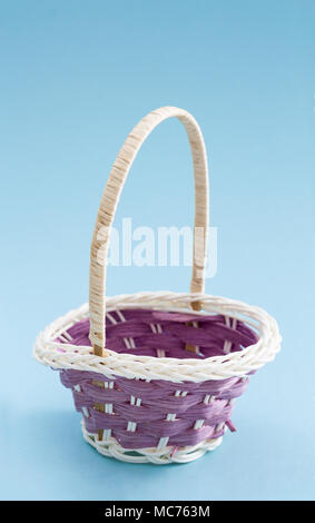 Small decorative empty wicker basket, on light blue background. Stock Photo