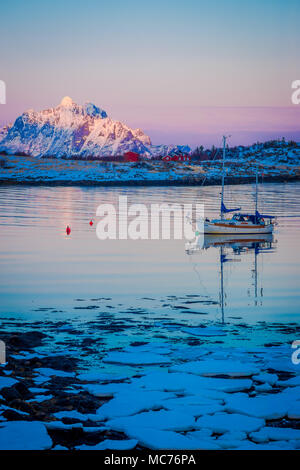 SVOLVAER, LOFOTEN ISLANDS, NORWAY - APRIL 10, 2018: Outdoor view of pieces of ice on the beach with a partial frozen lake with a boat sailing behind Stock Photo