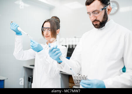 Couple of laboratory assistants in uniform working with analysis in test tubes at the medical laboratory Stock Photo