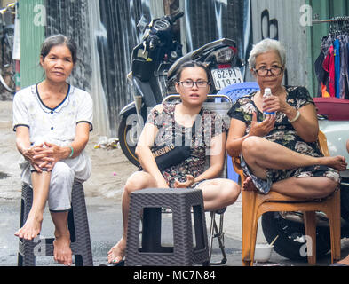 Three Vietnamese women sitting on plastic chairs on the pavement watching the street activities in Ho Chi Minh City, Vietnam. Stock Photo