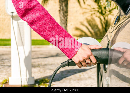 Woman plugs electric car to charging station in warm climate Stock Photo