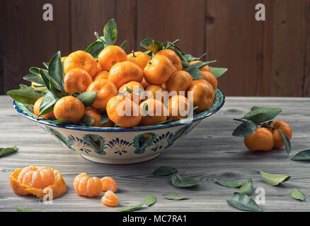 Fresh mandarins with leaves and slices in ceramic dish on textured gray wooden table. Natural day light. Healthy food concept. Stock Photo