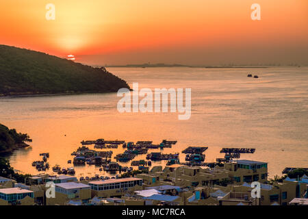 Small floating fishing farm and village houses on coastline. Beautiful seascape background at tropical sunset. China, Hong Kong. Stock Photo