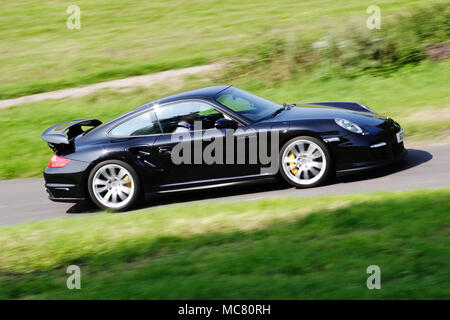 Profile (side view) of a black Porsche 911 997 Turbo driving fast on the public road. Stock Photo