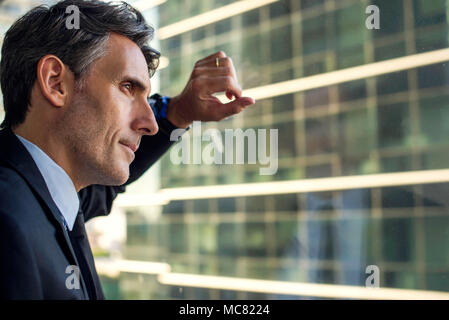 Man looking through window in high rise building Stock Photo
