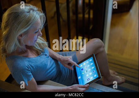 Mature woman sitting on stairs at home, using digital tablet Stock Photo