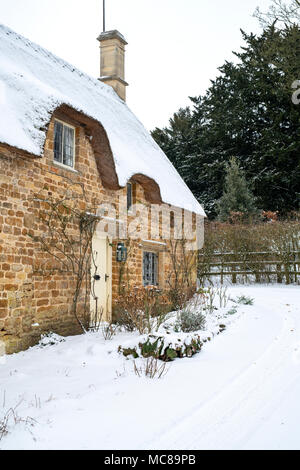 Thatched stone cottage in the winter snow. Great Tew, Cotswolds, Oxfordshire, England Stock Photo
