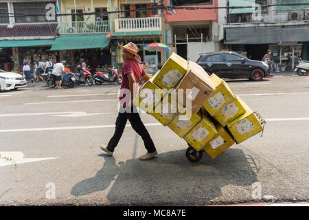 A worker in the Bangkok flower market pushes produce and goods on a sack barrow Stock Photo