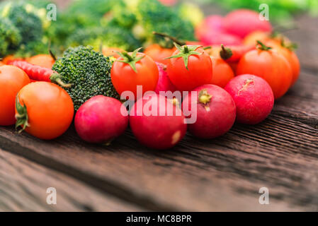 Close-up fresh radish, broccoli, tomatoes, peppers, and celery on dark wooden surface arranged in circle. Healthy diet concept, selective focus Stock Photo