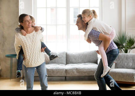 Laughing parents holding kids on back giving children piggyback ride playing together at home, cheerful family enjoying active funny game together, si Stock Photo