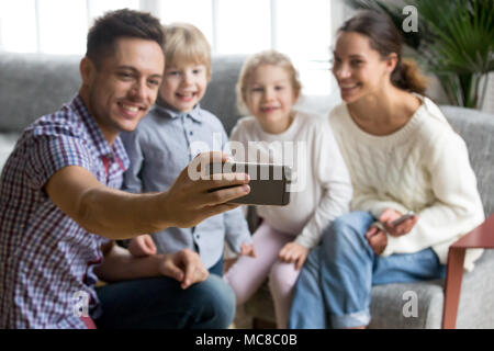 Smiling father holding smartphone taking selfie portrait of happy family with kids bonding together, husband making photo or shooting video of wife an Stock Photo