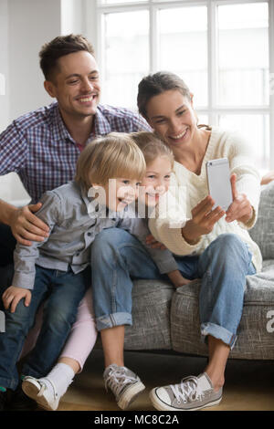 Happy mother taking family selfie with husband and kids looking at smartphone, playful adopted children siblings having fun posing for funny photo on  Stock Photo