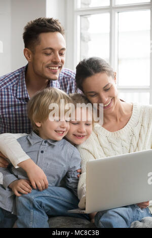 Happy family with adopted kids having fun using laptop together sitting on sofa, parents and son daughter relaxing at home with computer, smiling coup Stock Photo