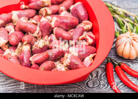 Fresh raw chicken hearts covered with pepper ready for cooking and garlic, pepper and herbs on table. Healthy diet concept. Selective focus. Stock Photo