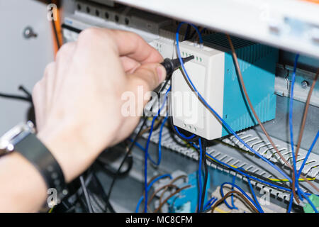 engineer hands installing electrical components in fuse box. Industry 4. Measuring voltage Stock Photo