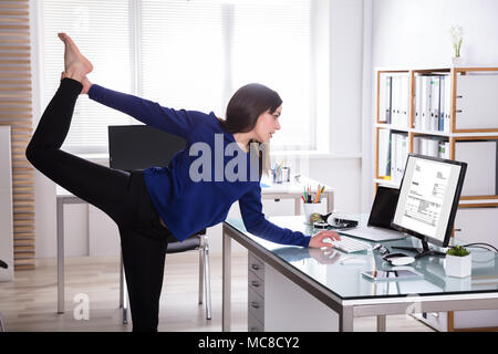 Young Businesswoman Looking At Invoice On Computer Doing Yoga Stock Photo