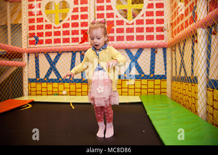 Happy little kid girl play in the playing room  jumping on the batute. Funny child having fun indoors. Stock Photo