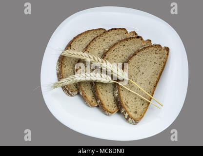 Sliced breads and cereal spikes on a white plate. Four slices of brown bread with decorative dry barley. Isolated on gray background. Stock Photo
