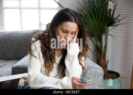 Sad girl feeling upset reading bad news in mobile message on smartphone at home, depressed frustrated young woman holds phone scared of threatening su Stock Photo
