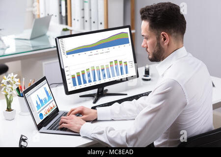 Side View Of A Young Businessman Analyzing Graphs On Laptop Stock Photo