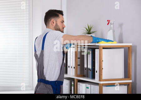 Close-up Of A Young Male Cleaner Cleaning Shelf At Workplace Stock Photo