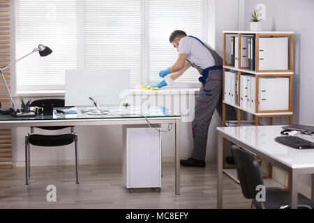 Young Male Janitor Cleaning The Window Sill With Sponge In Office Stock Photo