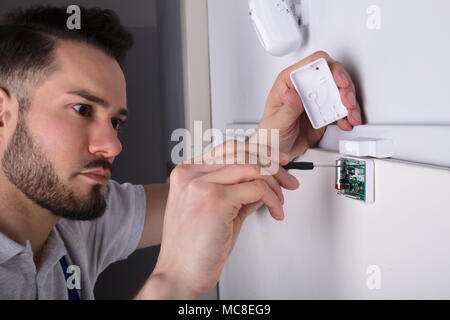 Young Male Technician Installing Security System Door Sensor On Wall Using Screwdriver Stock Photo