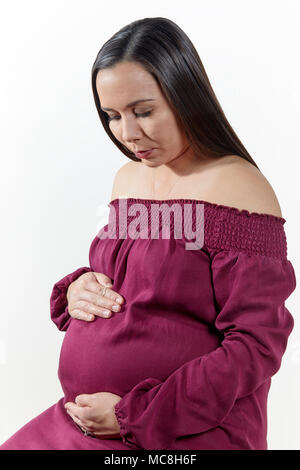 Attractive pregnant woman with her hands on her tummy sitting down isolated on white Stock Photo