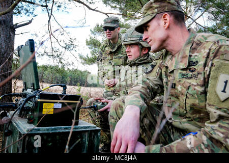 U.K. Lance Cpl. Tom Alexander (center), a combat engineer with the U.K. 22nd Engineer Regiment, 8th Engineer Brigade, shows U.S. Army Lt. Col. Jesse Curry (left) and Capt. Nick Hyde, both with the 82nd Brigade Engineer Battalion, 2nd Armored Brigade Combat Team, 1st Infantry Division, how to remotely operate a Terrier armored digger during a multinational joint equipment training exercise at Grafenwoehr Training Area, Germany, April 2, 2018, in preparation for a Robotic Complex Breach Concept demonstration. The Robotic Complex Breach Concept includes the employment of Robotic and Autonomous Sy Stock Photo